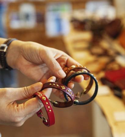 Close up of woman standing in a leather shop, holding leather bracelets.